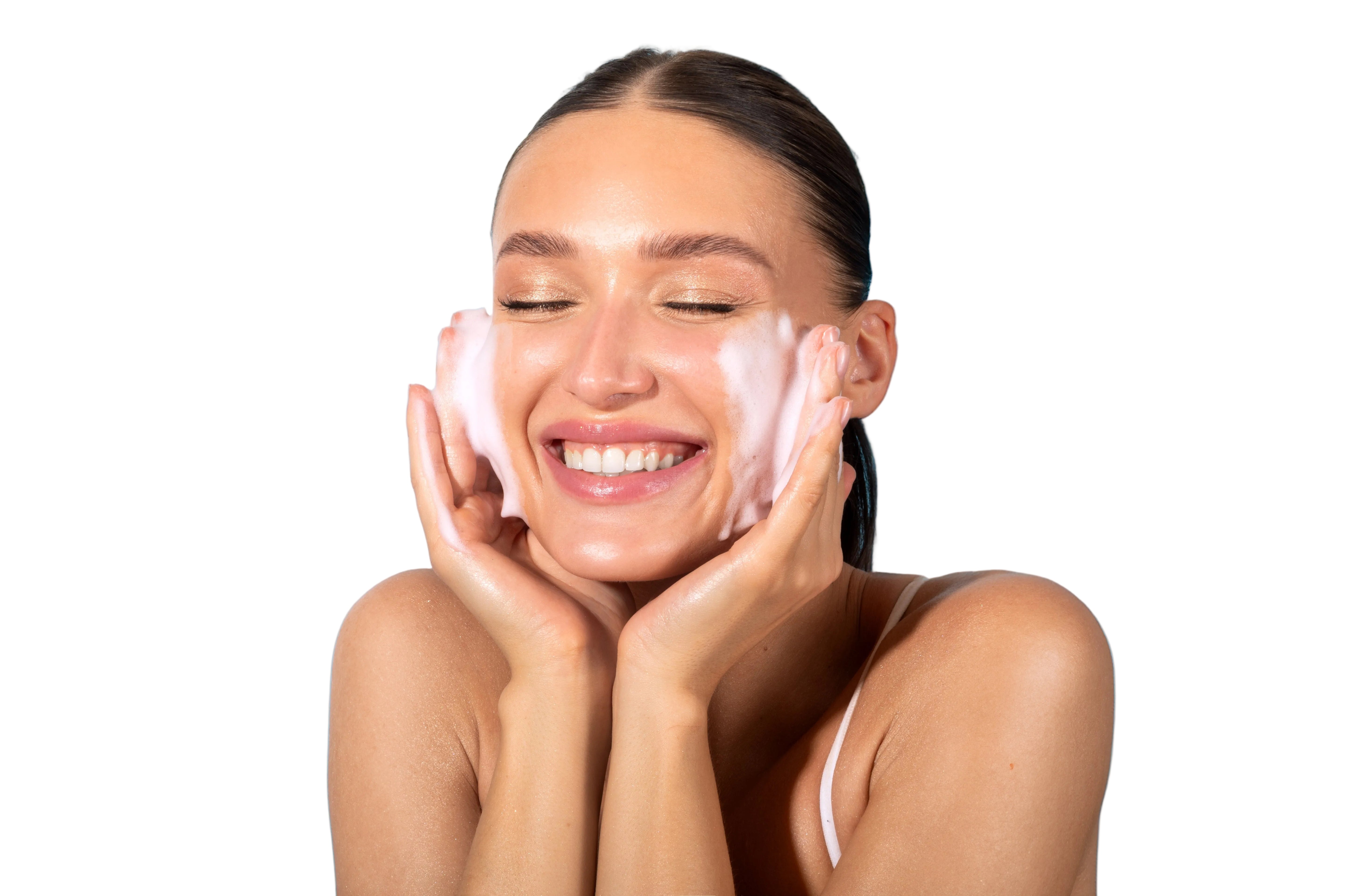 Woman smiling, applying facewash to her face on a white background