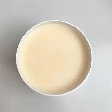 Flawless pro glow cleansing balm. lid off, light beige substance on a gray background, top view
