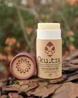 Kutis natural deodorant container with brown lid off a grassy background, front