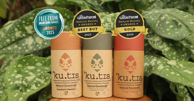 Three 'ku.tis' natural deodorant bottles with awards on a green leafy background