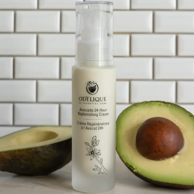 Odylique avocado-based skincare product avocado 24 hour replenishing cream with an avocado on a tiled background
