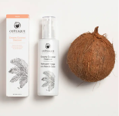 Odylique creamy coconut cleanser bottle with box and coconut. Frontal, light background