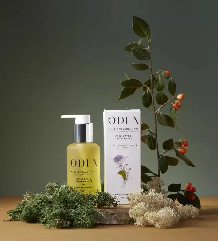 Bottle of ODEN skincare with white box on green background and leaves decoration.