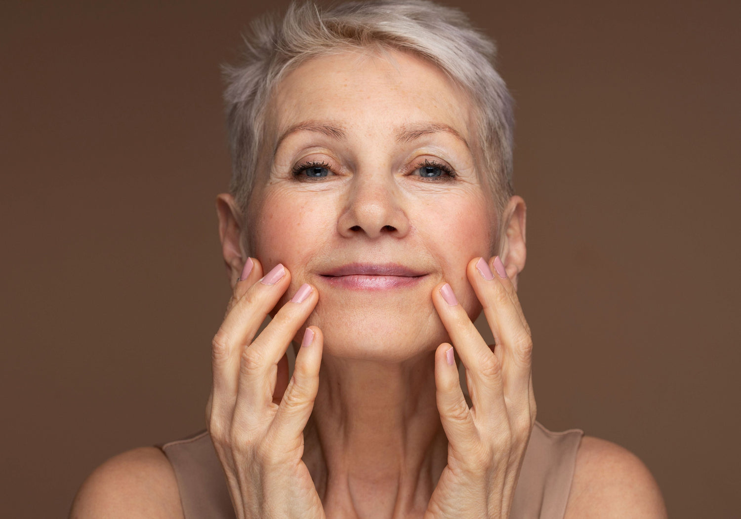 Mature lady smiling at the camera. Holding her face. Brown background