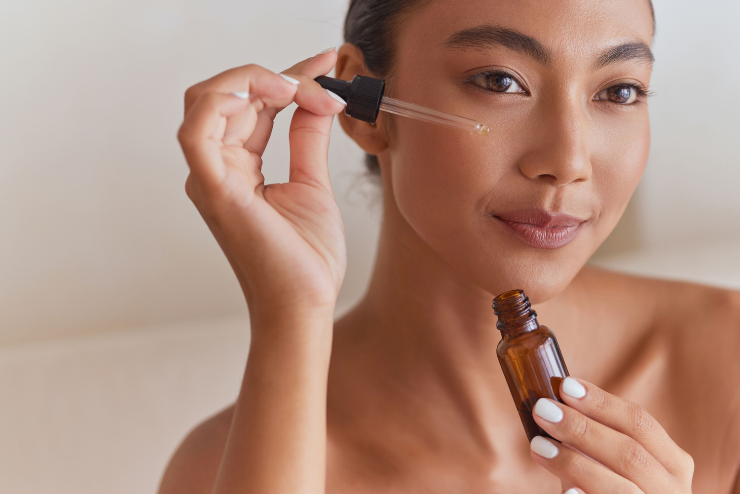 Lady applying face serum, beige background.