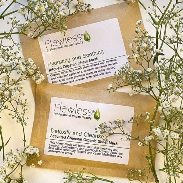 Two organic sheet mask packages from Flawless Professional Vegan Beauty surrounded by white flowers.