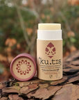 Kutis natural deodorant container with brown lid off a grassy background, front