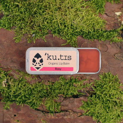 'ku.tis' organic lip balm in 'Rosy' color on a natural background with green moss. open
