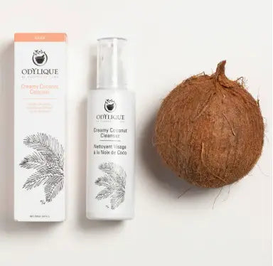 Odylique creamy coconut cleanser bottle with box and coconut. Frontal, light background