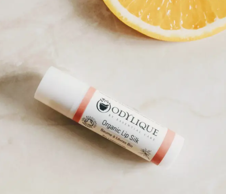 Lip balm with 'Odylique' branding on a light surface with a lemon slice in the background
