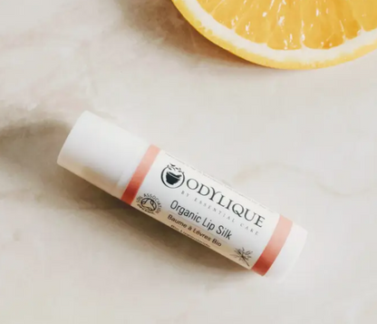 Lip balm with 'Odylique' branding on a light surface with a lemon slice in the background